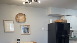 Una cocina con una mesa de comedor, sillas, un refrigerador negro y una lámpara en el techo.