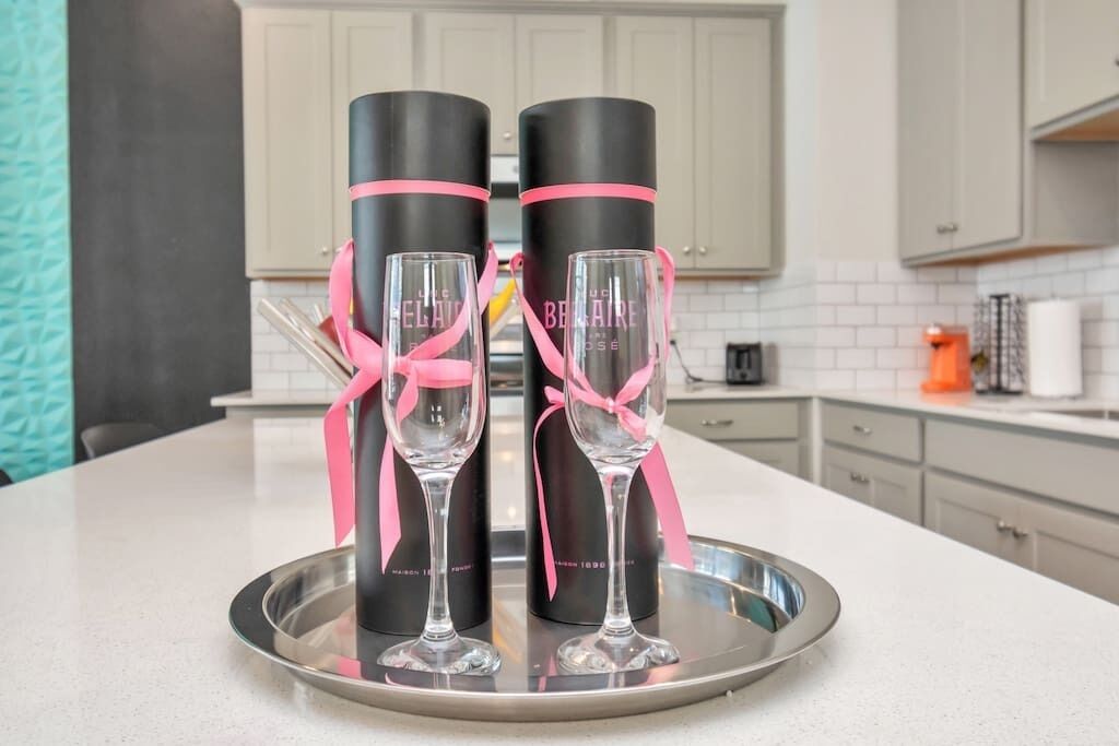 A kitchen counter with two champagne flutes and two black bottles with pink ribbons tied around them.