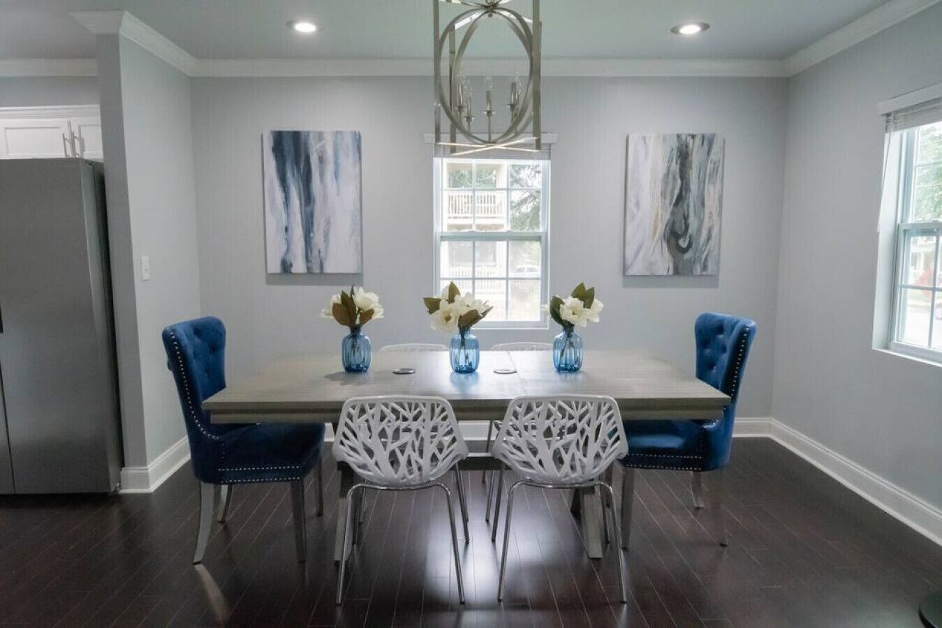 A dining area with a rectangular table, four chairs, and three vases with flowers.