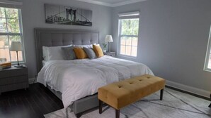 Una camera da letto con un letto grande, una panca, un comodino, una lampada e un quadro appeso al muro.
