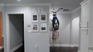 Un corridoio con pavimento in legno scuro, pareti bianche e una porta con la scritta "ATL". Sulle pareti sono appese delle foto incorniciate e una bicicletta.