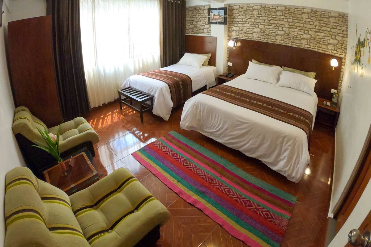 Ein Hotelzimmer mit zwei Betten, einem Sofa, einem kleinen Tisch und einem farbenfrohen Teppich.