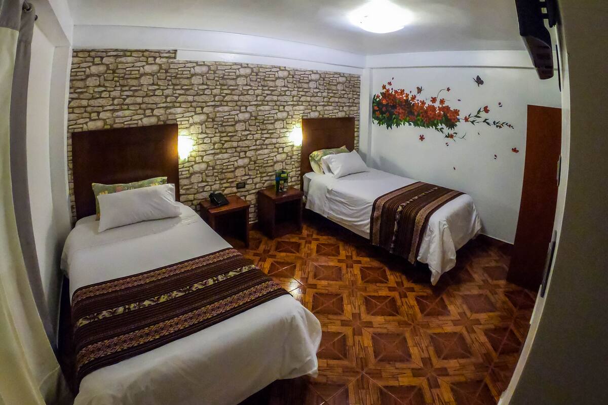 Ein Hotelzimmer mit zwei Betten, einer Steinwand, einem Holzboden und einer Wanddekoration mit floralem Muster.