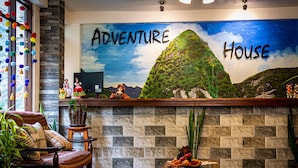 A reception area with a mural titled "Adventure House," a stone wall, a wooden reception desk, and a traditional chair. - Machu Picchu Adventure House (Machu Picchu)
