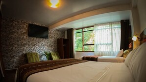 A bedroom with a stone wall, a bed, a sofa, a TV mounted on the wall, and a window with curtains. - Machu Picchu Adventure House (Machu Picchu)
