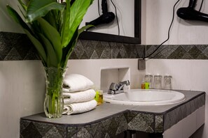 A bathroom with a sink, a mirror, a hairdryer, and a vase with green plants. - Machu Picchu Adventure House (Machu Picchu)