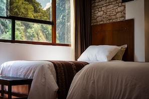 Ein Zimmer mit zwei Betten, einem Holzkopfende, einer Steinwand und einem Fenster mit Blick auf einen Wald.