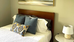 A neatly made bed with patterned pillows, a wooden headboard, and a painting of a landscape above it. - The Deannie - Entire 2 Bedroom Apt in Quilt Town, USA (Hamilton)