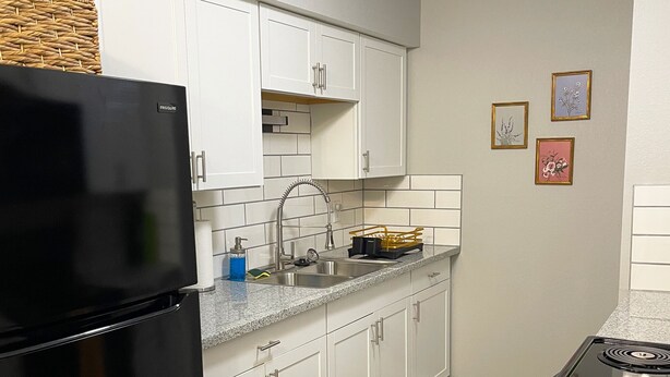A kitchen with white cabinets, a black refrigerator, a granite countertop, a stainless steel sink, and a stove. - The Deannie - Entire 2 Bedroom Apt in Quilt Town, USA (Hamilton)