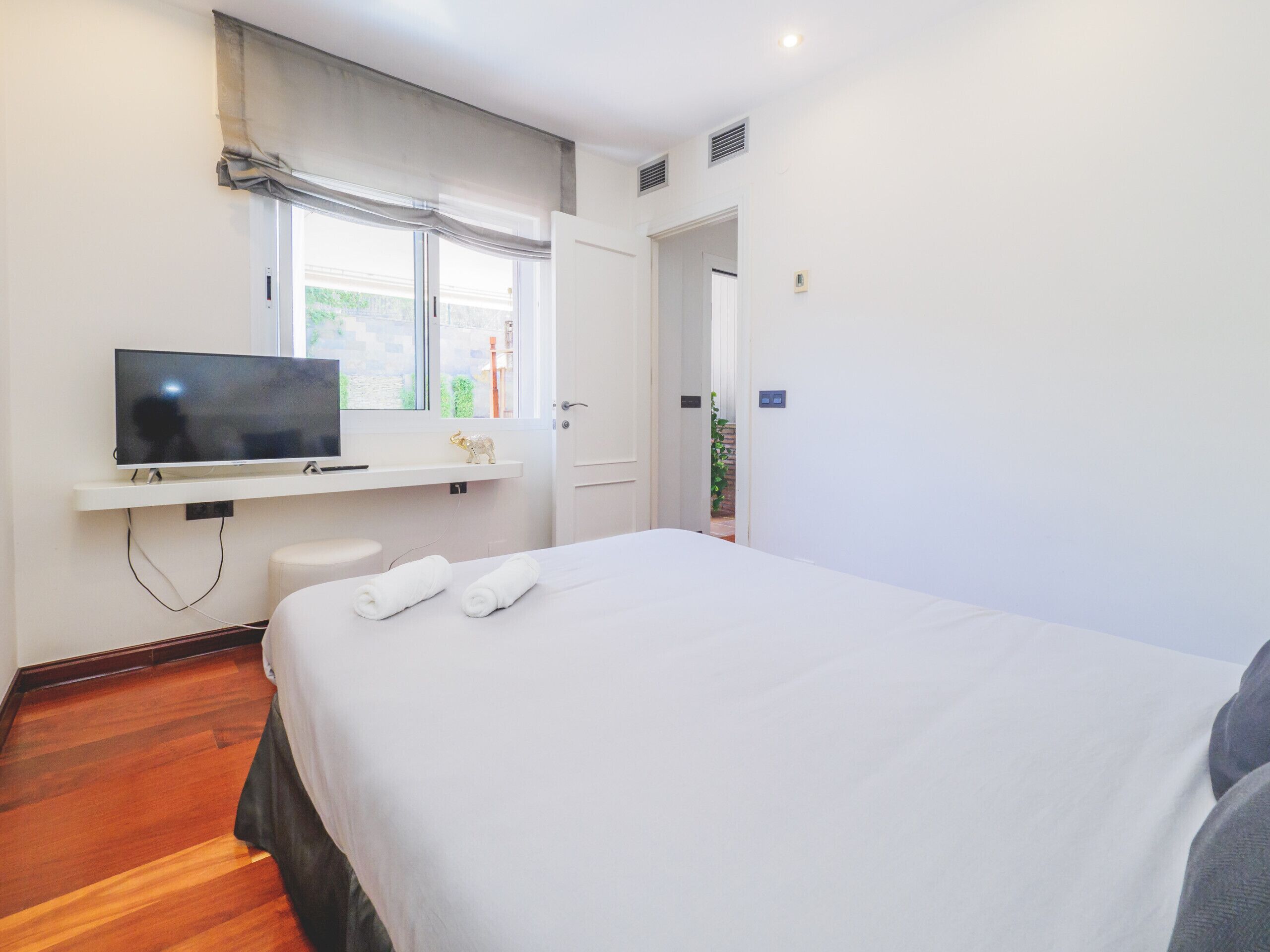 A hotel room with a bed, a TV on a shelf, and a window with curtains.
