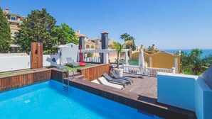 A rooftop swimming pool with lounge chairs and a wooden deck, overlooking a coastal area with buildings and trees. - Cubo's Gibralfaro House Center / private pool / air conditioning (Málaga)