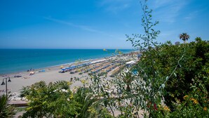 Une plage bordée de rangées de parasols et de chaises longues, un ciel bleu azur et l’océan en toile de fond.