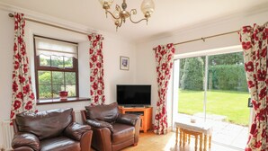A living room with two leather sofas, a wooden coffee table, a TV on a stand, and a sliding glass door leading to a garden. - Tilladavin House (Kilmore)