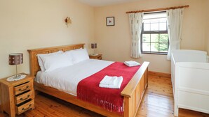 A bedroom with a wooden bed, a nightstand, a lamp, a window with curtains, and a view of greenery outside. - Tilladavin House (Kilmore)