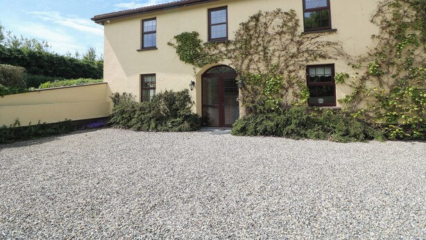 A two-story building with a gravel driveway, a large arched entrance, and a chimney. - Tilladavin House (Kilmore)
