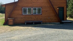 Una cabaña de madera con techo triangular, una puerta principal y tres ventanas.