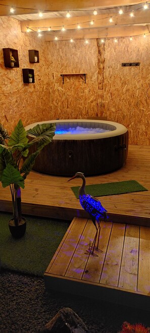 Un área de spa con una bañera de hidromasaje, suelo de madera e iluminación decorativa.