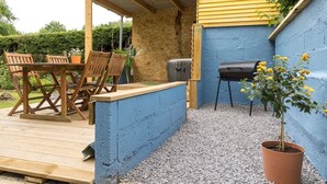 A covered patio area with a wooden table and chairs, a barbecue grill, and a potted plant. - Maison Avec Jacuzzi, Calme ET Detente EN Nature (Chepy)