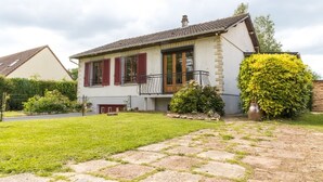 A two-story house with a balcony, a well-maintained lawn, and a large bush. - Maison Avec Jacuzzi, Calme ET Detente EN Nature (Chepy)