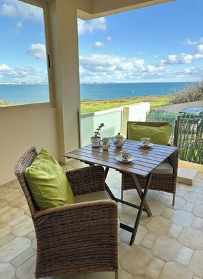 Een balkon met rieten meubilair, een tafel met theeservies, en uitzicht op zee.
