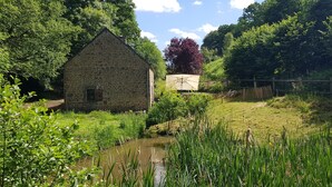 A stone building with a small pond in front, surrounded by lush greenery and trees. - Nature cottage in Suisse Normande (Athis Val de Rouvre)