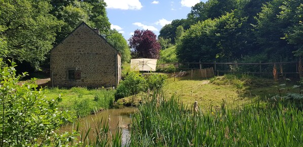 A stone building with a small pond in front, surrounded by lush greenery and trees. - Nature cottage in Suisse Normande (Athis Val de Rouvre)