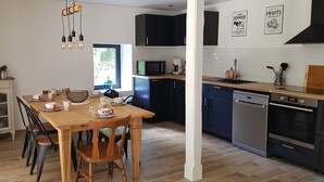 A modern kitchen with dark cabinets, a wooden dining table, and a built-in oven. - Nature cottage in Suisse Normande (Athis Val de Rouvre)