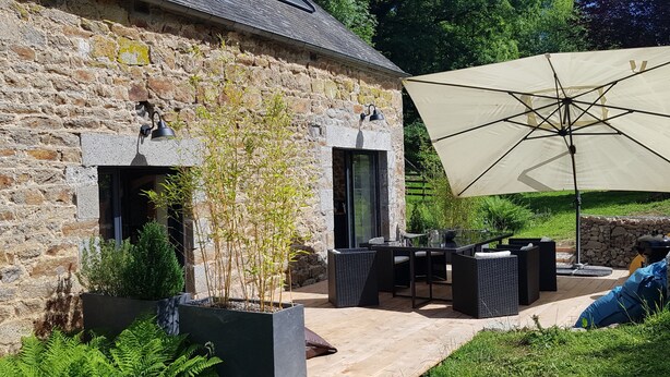 A stone building with a patio area featuring outdoor furniture and a large umbrella. - Nature cottage in Suisse Normande (Athis Val de Rouvre)