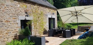A stone building with a patio area featuring outdoor furniture and a large umbrella. - Nature cottage in Suisse Normande (Athis Val de Rouvre)