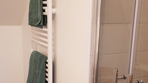 A bathroom with a glass shower door, a white towel rack with two green towels, and a green rug on the floor. - Nature cottage in Suisse Normande (Athis Val de Rouvre)