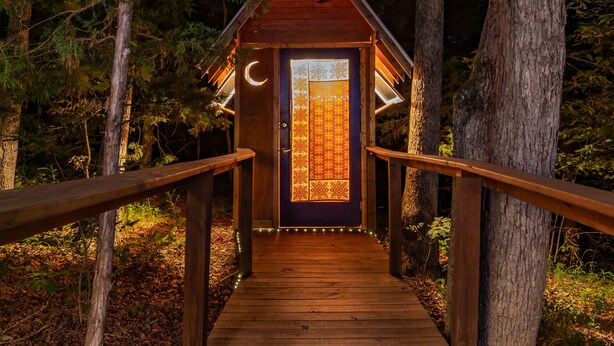 A wooden pathway leading to a small cabin with a glass door and a crescent moon design. - Yurt Floating in the Forest (Holts Summit)
