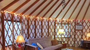 A cozy interior with a wooden-framed sofa, two lamps, wicker chairs, and a small round table. - Yurt Floating in the Forest (Holts Summit)