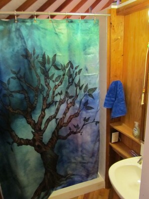 A bathroom with a tree-themed shower curtain, a wooden vanity, and a white sink. - Yurt Floating in the Forest (Holts Summit)