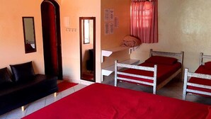 A room with a black sofa, two single beds with red bedding, a mirror, and a red curtain. - Pousada Villa Garden (São Sebastião)