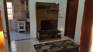 A compact living space with a kitchenette, a flat-screen TV, and a patterned rug. - Pousada Villa Garden (São Sebastião)