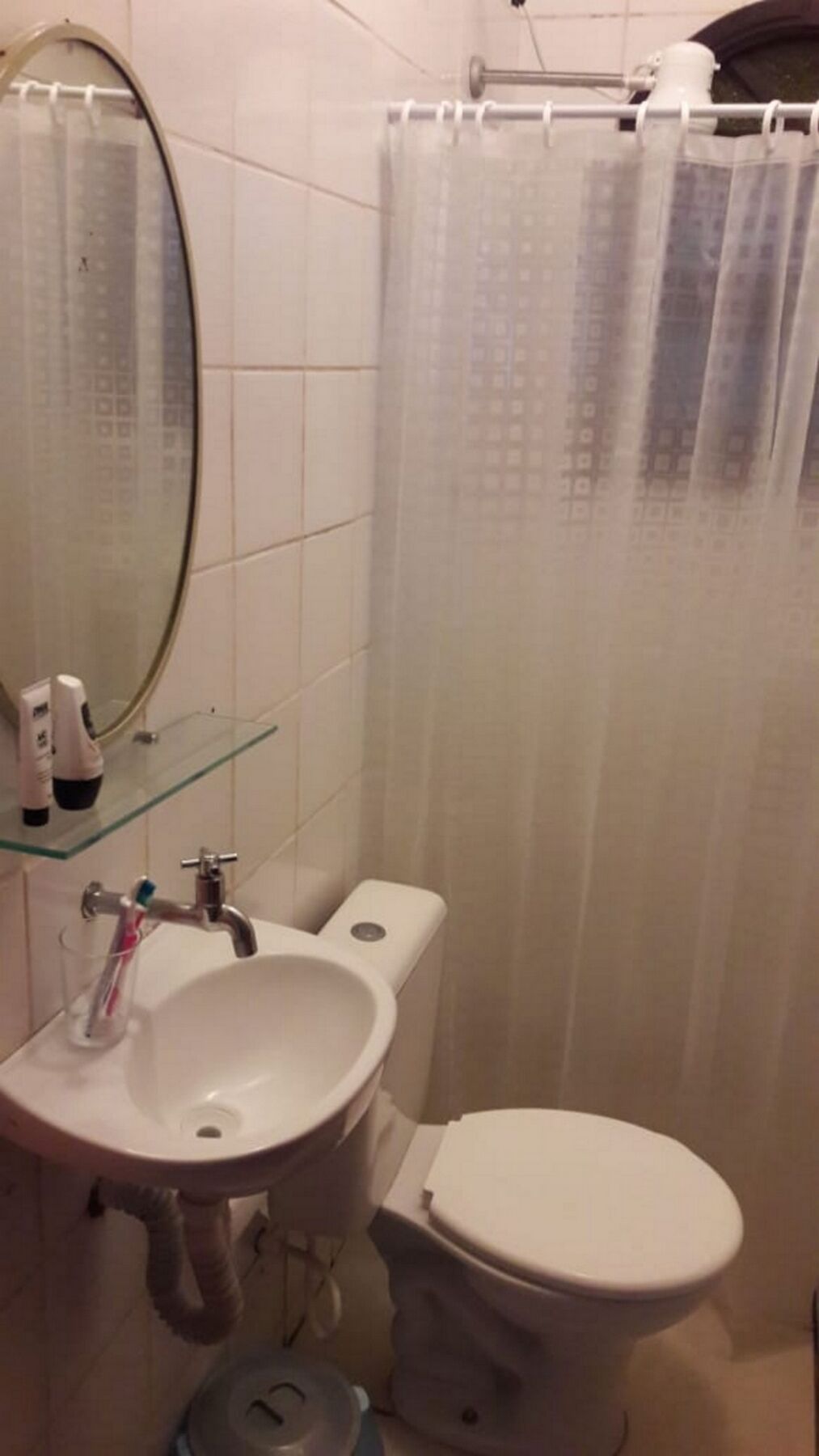 A bathroom with a white sink, mirror, and toilet. There is a glass shelf above the sink with toiletries.