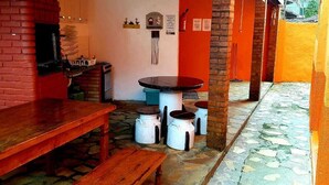 A rustic outdoor seating area with a brick fireplace, a wooden bench, a round table, and white buckets. - Pousada Villa Garden (São Sebastião)