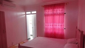 Une pièce avec un lit, une fenêtre ornée de rideaux roses et une porte donnant sur une autre pièce.