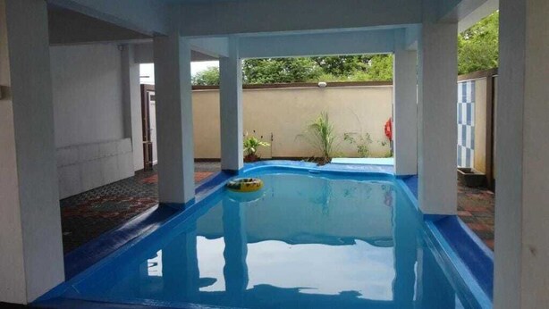Une piscine intérieure au sol bleu, entourée de piliers blancs et offrant une vue sur un jardin extérieur.