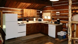 A rustic cabin-style kitchen with wooden walls, a refrigerator, stove, microwave, sink, and a coffee maker. - Gold Camp - A Classy-Rustic Gem (Clark)