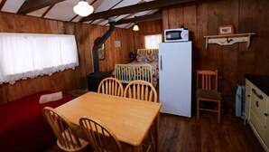 L’intérieur chaleureux d’un chalet comprend une table à manger en bois, des chaises, un canapé rouge, un réfrigérateur blanc, un four à micro-ondes et un petit coin cuisine avec un évier et des placards.