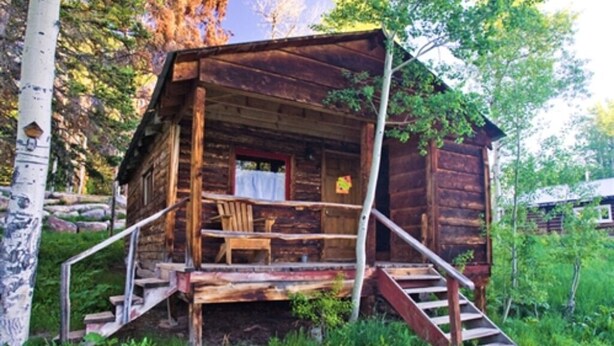 Une cabane en bois rustique, dotée d’une véranda, d’une table et d’une chaise.