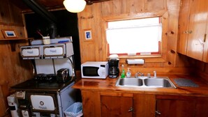 A compact kitchen with wooden cabinets, a stove, a microwave, and a sink. - Beaver Cabin - Cozy rustic cabin (Clark)