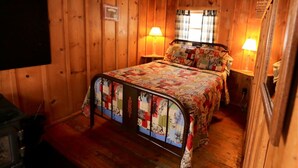 A wooden cabin bedroom with a metal bed frame, two bedside lamps, and a window with curtains. - Beaver Cabin - Cozy rustic cabin (Clark)