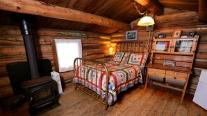 A cozy log cabin room with a bed, a wooden dresser, a small table, and a fireplace. - Honeymoon Cabin - A Romantic 2 Person Cabin (Clark)
