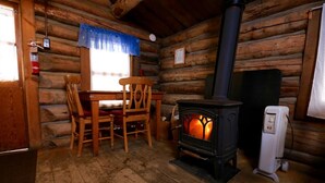 A log cabin interior with a wood-burning stove, a dining table with chairs, and a white heater. - Honeymoon Cabin - A Romantic 2 Person Cabin (Clark)