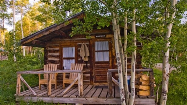 A rustic log cabin with a porch, wooden chairs, and a table. - Honeymoon Cabin - A Romantic 2 Person Cabin (Clark)