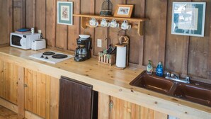 A kitchen with wooden cabinets, a microwave, a coffee maker, and a sink. - Bakers Cabin - A Cozy Rustic One-Room Cabin (Clark)