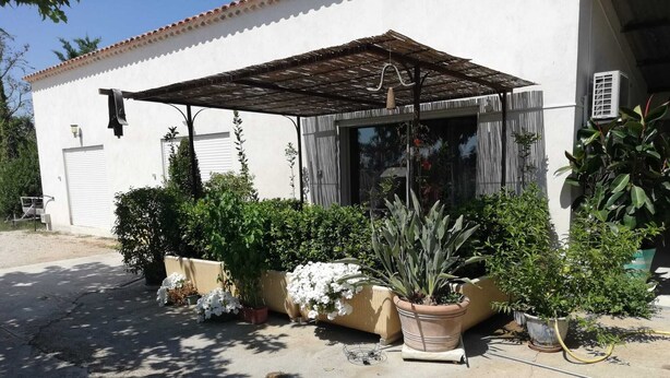 A white building with a covered patio area, potted plants, and a hanging light fixture.