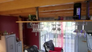A cozy room with a wooden ceiling, a dining table with chairs, a sofa with red cushions, and a window with curtains.